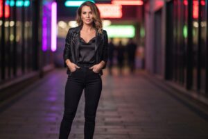 Kobieta w czarnej skórzanej kurtce i ciemnych jeansach w miejskim nocnym otoczeniu z neonowymi światłami